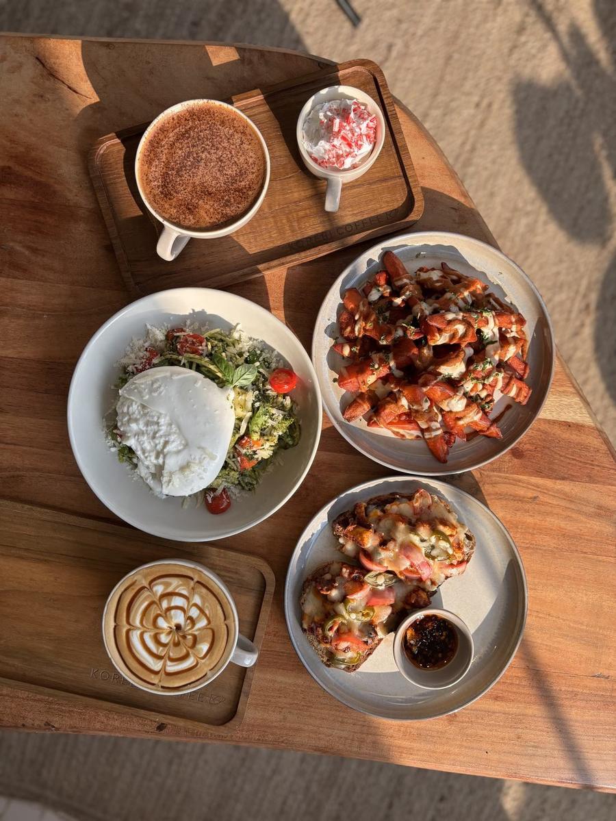 Overhead view of coffee, burrata salad, loaded fries and toast on a wooden table